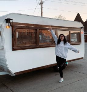 Person standing in front of a trailer outfitted to serve coffee. 