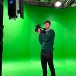 Eli Delhay holding a camera in front of a green screen.