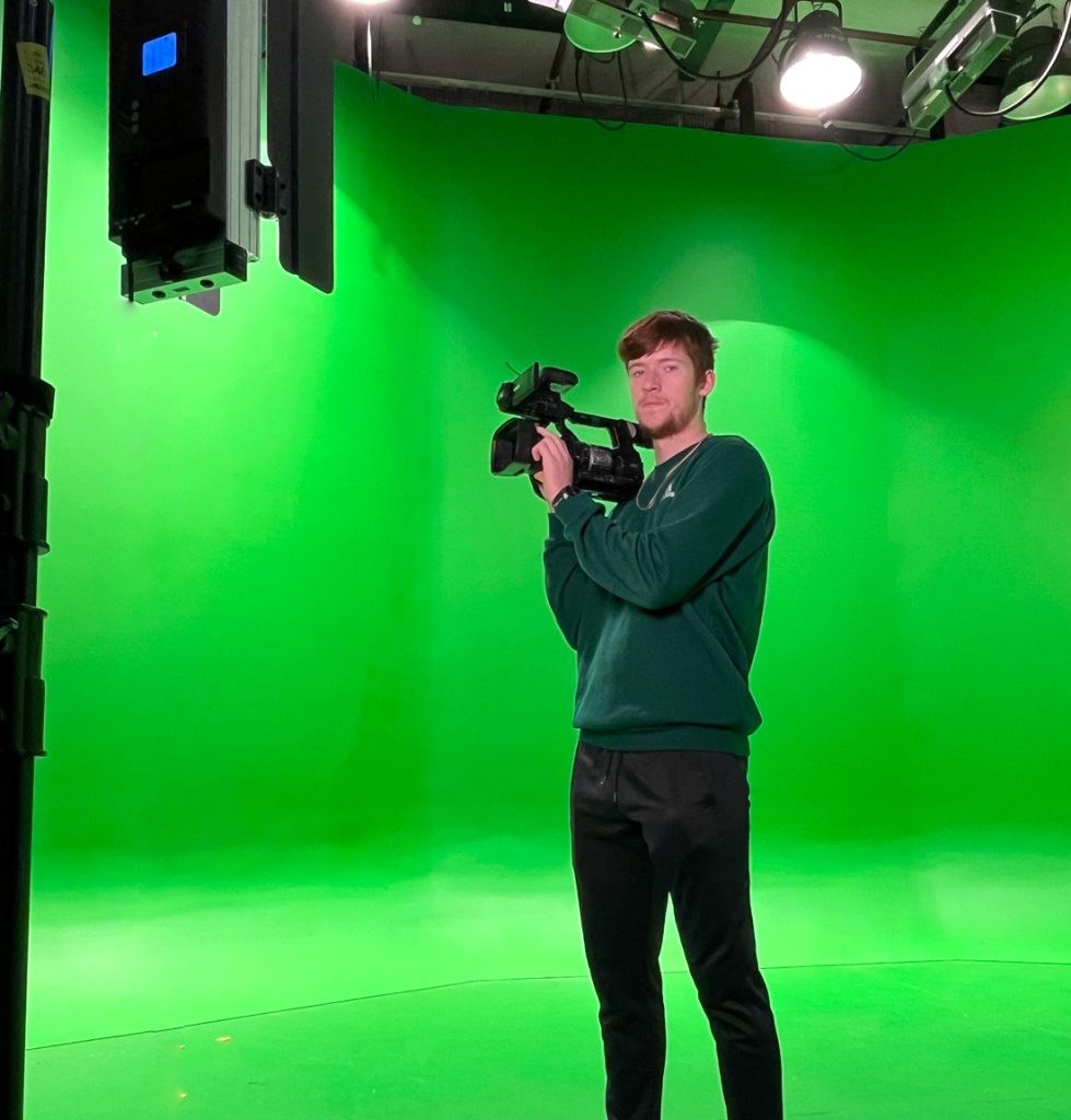 Eli Delhay holding a camera in front of a green screen.