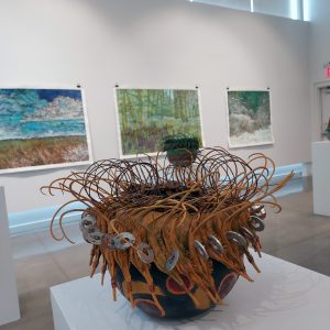 A photo of a gallery exhibition, focusing on a piece of basket-style art.