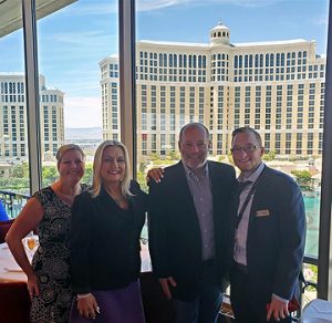 Four people standing in front of a window that overlooks a hotel.