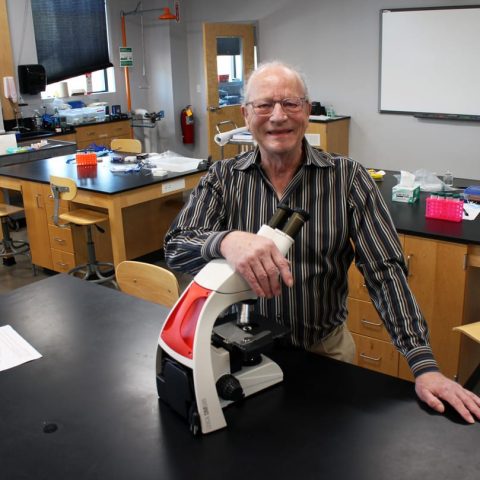 Dr. John Bohmfalk in a lab with a microscope.