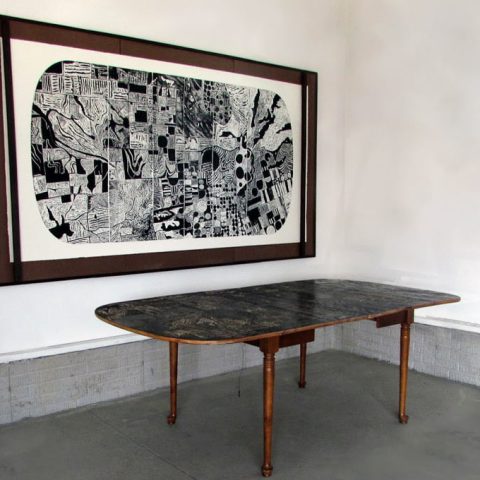 Lauren Feden explores landscape through the medium of printmaking by carving agricultural patterns onto wooden furniture — both by hand and and using more advanced tools as a metaphor for farming. The print from the carving is hanging on the wall by the table.