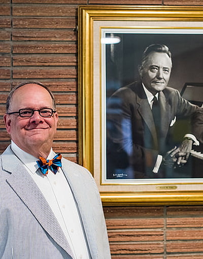 Photo of Robin Koozer standing next to a framed portrait of Hayes M. Fuhr.